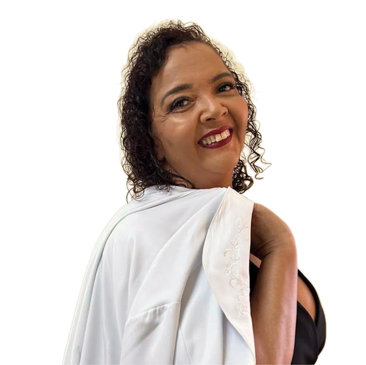 Cris Souza sorrindo, de cabelo cacheado solto, olhando por cima do ombro com o jaleco branco bordado apoiado nele.